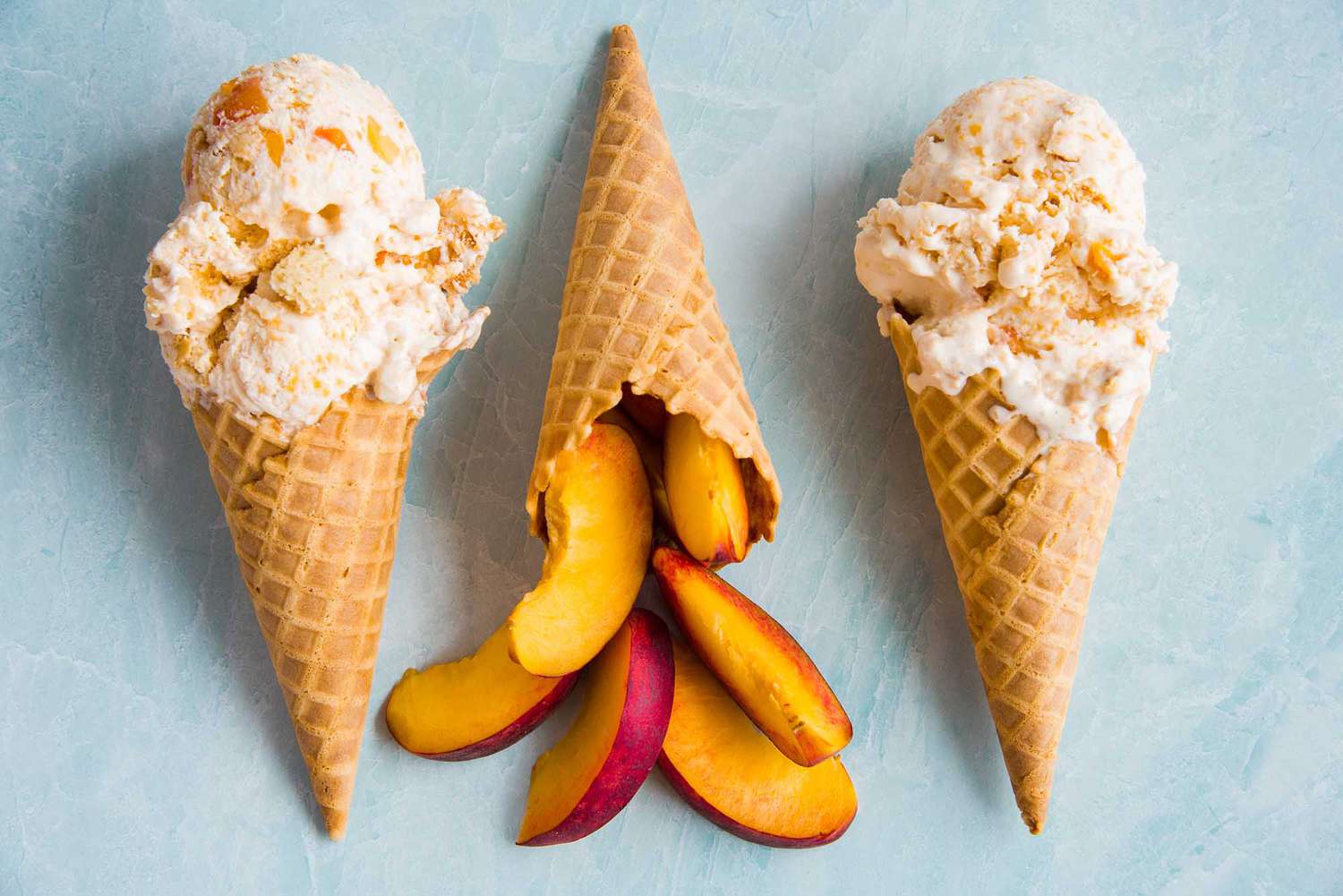 Two homemade peach cobbler ice cream cones are set on either side of a cone with sliced peaches.
