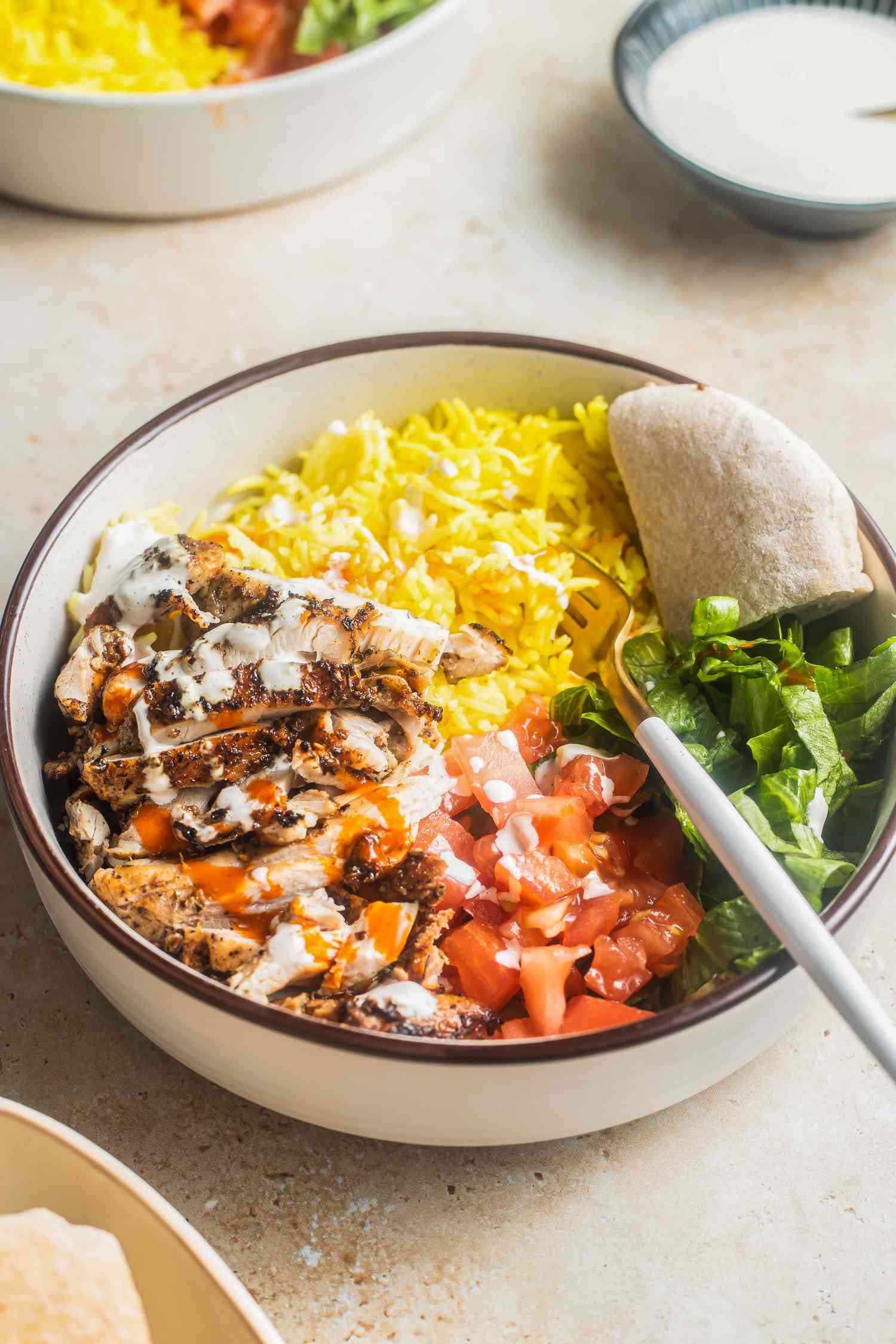  Bowl of Halal Cart-Style Chicken Over Rice Next a Bowl of Dressing and Another Bowl With Another Serving