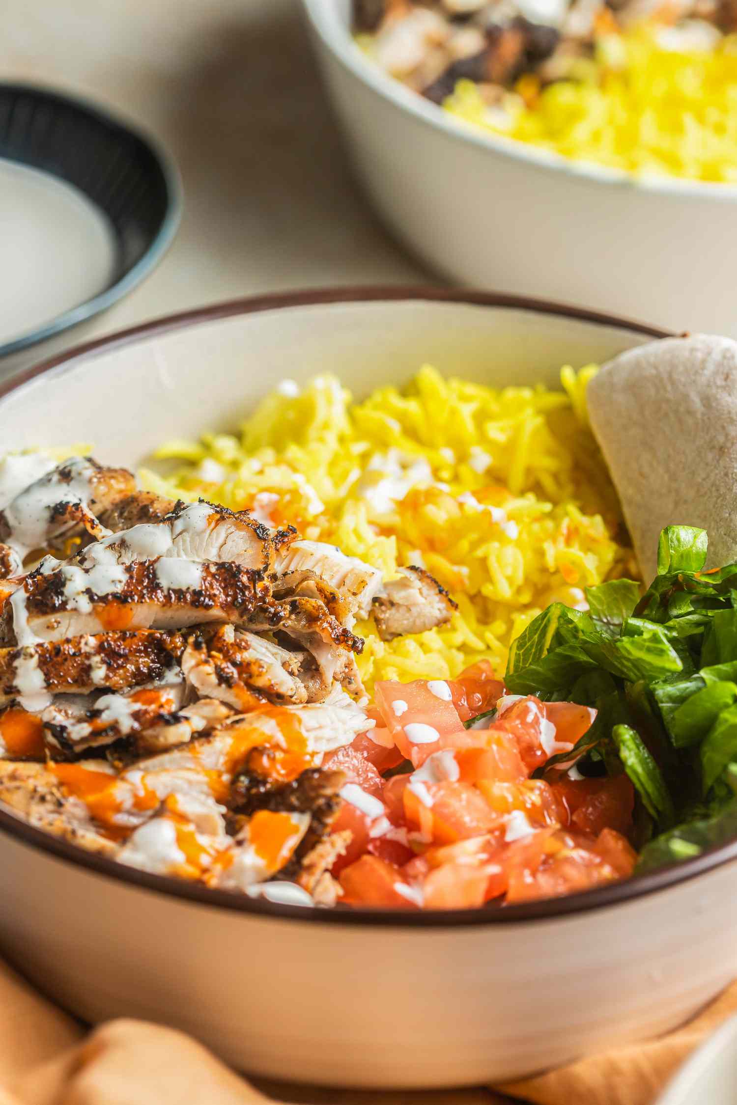 Bowl of Halal Cart-Style Chicken Over Rice, and in the Background, Another Serving in a Bowl and a Bowl of Dressing